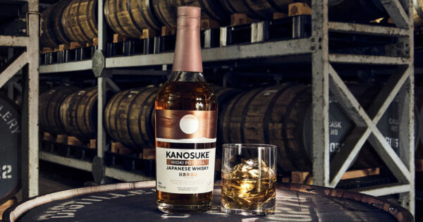 eine Flasche Kanosuke Hioki Pot Still nebst Glas auf einem Holzfass