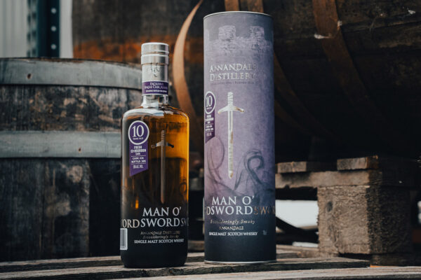eine Flasche Annandale 10 Jahre Man O‘Sword Single Cask nebst Geschenkhülle, umgeben von Holzfässern