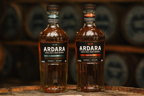 zwei Flaschen Whiskey stehen auf einem Holzfass in einem Fasslager