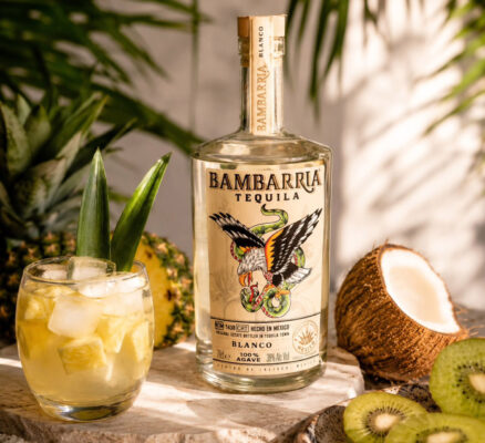 Bambarria Blanco eine Flasche Bambarria Blanco auf einer Steinplatte, daneben ein Drink, eine Kokosnuss, Kiwis und eine Ananas