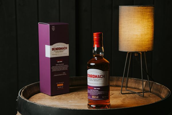 Benromach Contrasts: Port Cask Finish eine Flasche Benromach Contrasts: Port Cask Finish, eine Geschenkverpackung und eine Lampe auf einem Holzfass