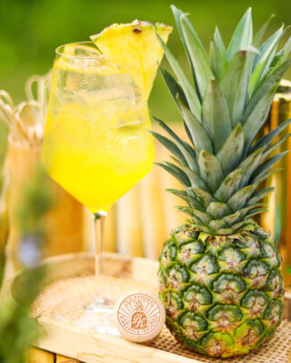 Big Kahuna Spritz das Foto zeigt einen Drink nebst Ananas auf einem Holzbrett