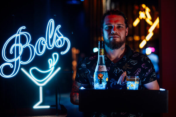 das Foto zeigt einen Mann, vor ihm ein Drink und eine Flasche, links eine Neonreklame