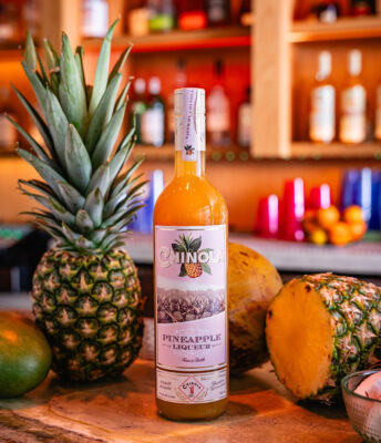 eine Flasche Chinola Pineapple, umgeben von Ananas, auf einem Bartresen