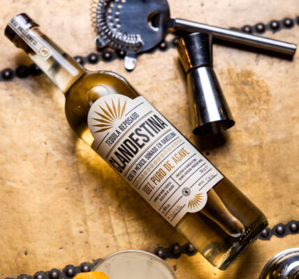 eine Flasche Clandestina Reposado liegt auf einer Kiste, umgeben von Barutensilien