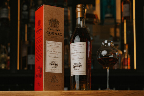 Cognac François Voyer Grande Champagne Réserve Ancestral for Kirsch Import eine Flasche Cognac François Voyer Grande Champagne Réserve Ancestral for Kirsch Import nebst Verpackung und Glas auf einem Bartresen