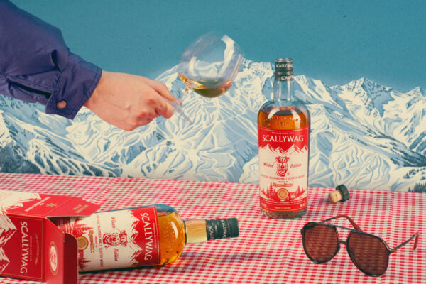 Scallywag Winter Edition 2026 eine Flasche Scallywag Winter Edition 2026 steht auf einem Tisch, eine weitere liegt. Eine Hand ragt mit einem Glas in das Foto