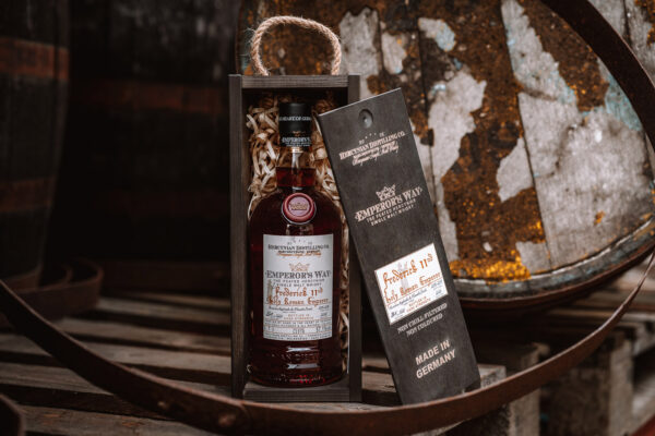 eine Flasche Emperor’s Way Frederick II in eienr Holzkiste, umgeben von Holzfässern