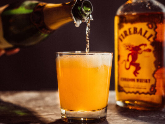 das Foto zeigt den Drink "Man-mosa", in den gerade Champagner geschüttet wird. Daneben eine Flasche Fireball Liqueur