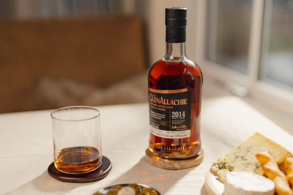 The GlenAllachie Sinteis Part III eine Flasche The GlenAllachie Sinteis Part III nebst Glas und umgeben von Käse sowie Oliven