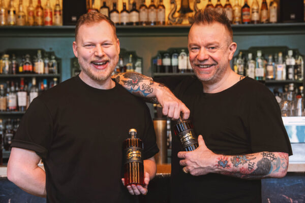 das Foto zeigt zwei Männer in einer Bar. In ihren Händen Flaschen Golden Bitter Aperitivo di Monaco