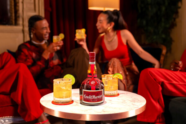 eine Flasche Grand Marnier Cordon Rouge nebst Drinks auf einem Tisch. Drum herum Menschen in roter Kleidung