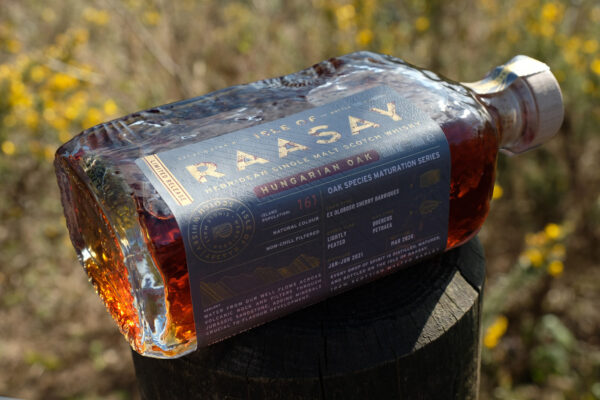 eine Flasche Isle of Raasay Hungarian Oak liegt auf einem Holzstamm im Grünen