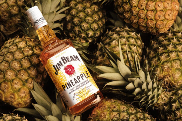 eine Flasche Jim Beam Pineapple liegt auf einem Haufen Ananas
