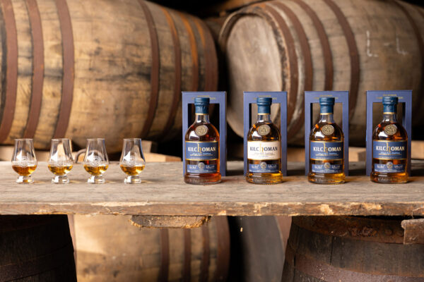 Kilchoman Family Collection vier Gläser und vier Flaschen Whisky stehen auf einem Holztisch in einem Fasslager