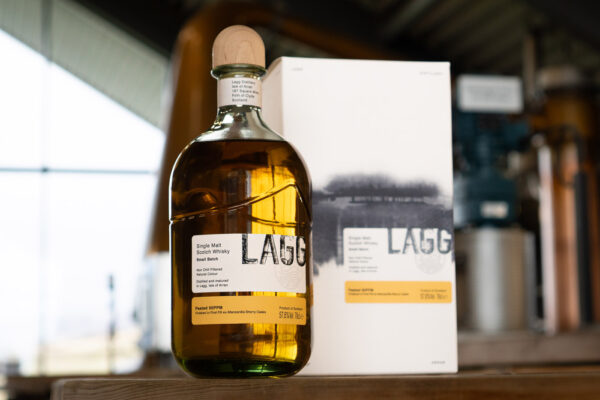 eine Flasche Lagg Small Batch Manzanilla Cask Finish neben einer Geschenkverpackung inmitten einer Brennerei