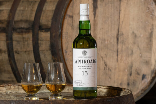 Laphroaig 15 Jahre eine Flasche Laphroaig 15 Jahre nebst Gläsern auf einem Holzfass, im Hintergrund ein weiteres Holzfass