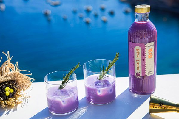 Lav'a Belle Rêve Doux eine Flasche Lav'a Belle Rêve Doux und zwei Gläser stehen auf einem weißen Tisch an einer Klippe zum Meer
