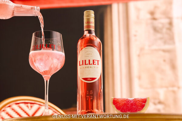 das Foto zeigt eine Flasche Lillet Rosé nebst einem Glas des Drinks "Lillet Rosé Spritz mit Grapefruit Limonade"