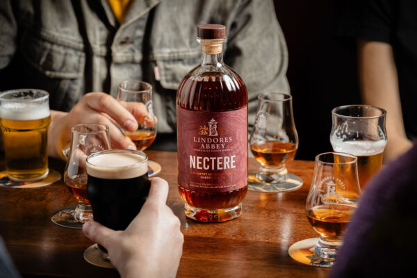 eine Flasche Lindores Abbey Nectere steht inmitten eines Tischs, darum Menschen Gläsern