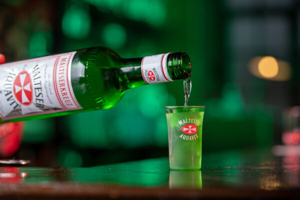Malte. Kurze Klarheit. Malteserkreuz Aquavit wird aus einer Flasche in ein geeistes Shotglas eingeschenkt