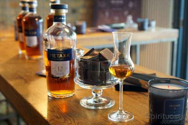 Metaxa 12 Sterne x Chocolate Pairing Flaschen Metaxa 12 Sterne, ein Gefäß mit Schokolade, ein Glas und eine Kerze stehen auf einem Holztisch