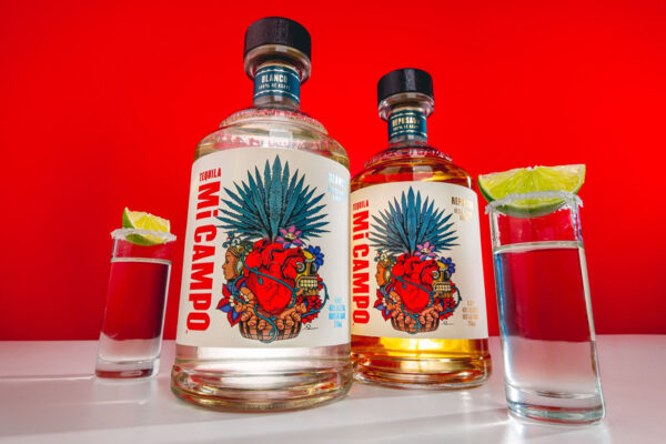 Mi Campo Tequila zwei Flaschen und Shots stehen vor einer roten Wand