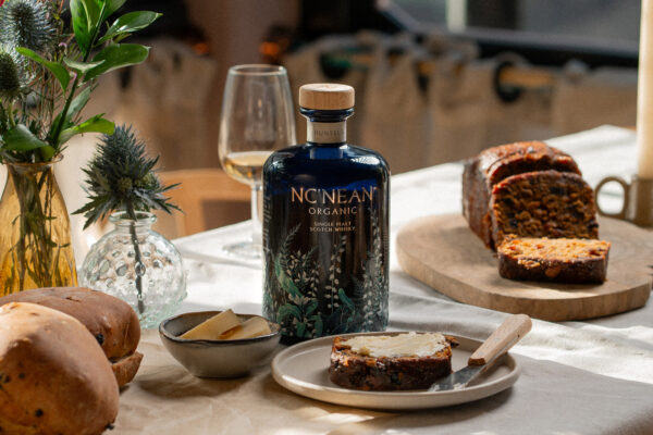 das Foto zeigt eine Flasche Nc'nean Huntress 2026 auf einem mit frisch gebackenem Kuchen gedeckten Esstisch