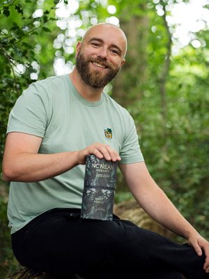 Nc’nean Quiet Rebels - Matthew ein Mensch befindet sich mit einer Geschenkhülle Whisky im Wald