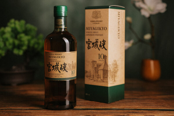 das Foto zeigt eine Flasche Nikka Miyagikyo 10 Jahre nebst Geschenkverpackung auf einem Holzboden. Im Hintergrund japanischen Blumen