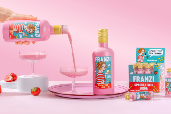 Franzi Spaghettieis-Likör Flaschen Franzi Spaghettieis-Likör, Gläser und Erdbeeren vor rosafarbenem Grund