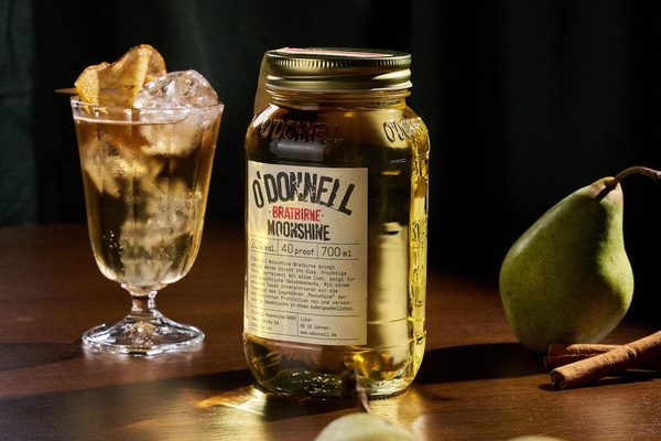 O'Donnell Moonshine Bratbirne ein Einmachglas O'Donnell Moonshine Bratbirne steht neben einem Glas, einer Birne und Zimtstangen auf einem Tisch