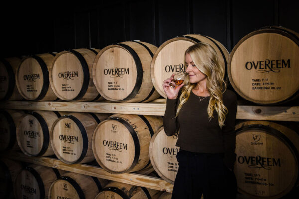 Jane Overeem Jane Overeem riecht an einem Glas Whisky und steht vor einem Fassstapel