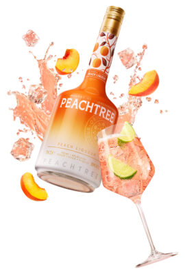 Peachtree eine Flasche Peachtree und ein Glas. Dazwischen Flüssigkeit und Pfirsichschnitze