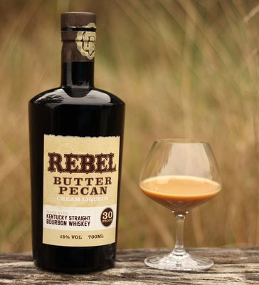 Rebel Butter Pecan Cream Liqueur eine Flasche Rebel Butter Pecan Cream Liqueur und ein Glas auf einem Holztisch im Freien