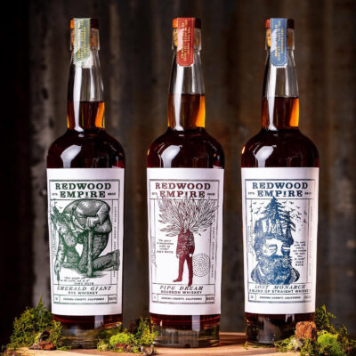 das Foto zeigt drei Flaschen Redwood Empire Whiskey auf einer Baumscheibe