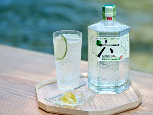 eine Flasche Roku Gin Noryo Tea Edition nebst Drink auf einem Holztablett