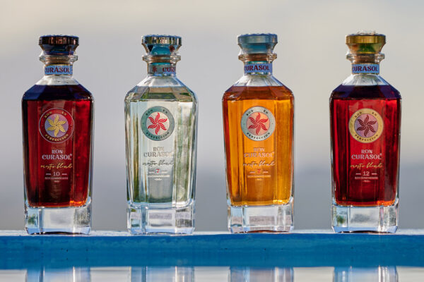 vier Flaschen Ron Curasol auf einem blauen Podest vor Wasser