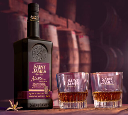 Saint James Nectar du Maître de Chai eine Flasche Saint James Nectar du Maître de Chai nebst zweier Gläser. Im Hintergrund Fassstapel