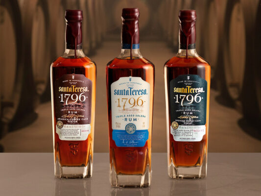 Santa Teresa 1796 drei Flaschen Rum stehen auf einem Tisch, im Hintergrund ein Bild von Holzfässern