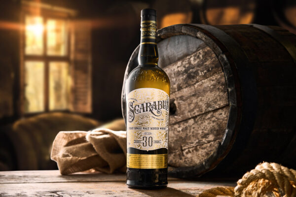 Scarabus 30 Jahre Batch No. 2 eine Flasche Scarabus 30 Jahre Batch No. 2 auf einem Holztisch, im Hintergrund ein Holzfass