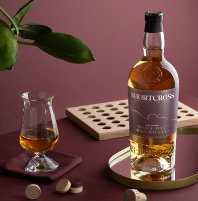 Shortcross Peated Single Malt 5 Jahre eine Flasche Shortcross Peated Single Malt 5 Jahre auf einem Tablett, daneben ein Glas