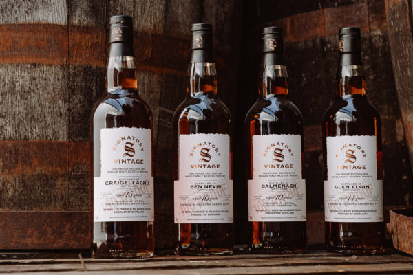 Signatory Vintage 100 Proof Editions vier Flaschen Whisky stehen vor Holzfässern