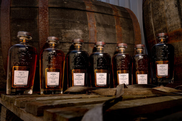 Signatory Vintage Cask Strength Collection sieben Flaschen Whisky stehen auf einer Palette, umgeben von Holzfässern