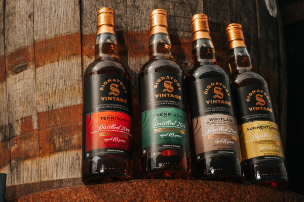 Signatory Vintage The Un-Chillfiltered Collection vier Flaschen Whisky stehen vor einem Holzfass