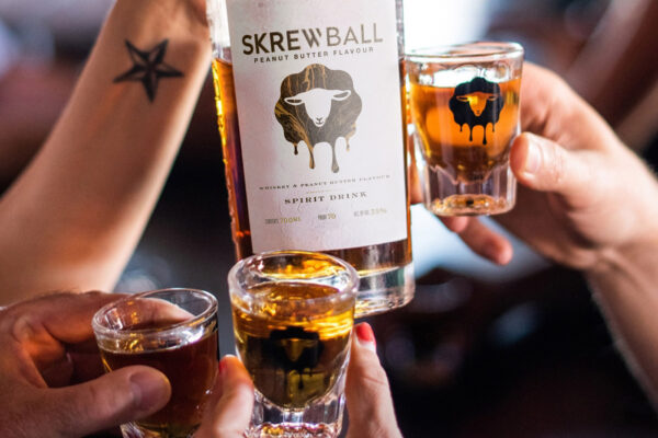 eine Flasche Skrewball Peanut Butter Flavour, Menschen stoßen mit Shots an