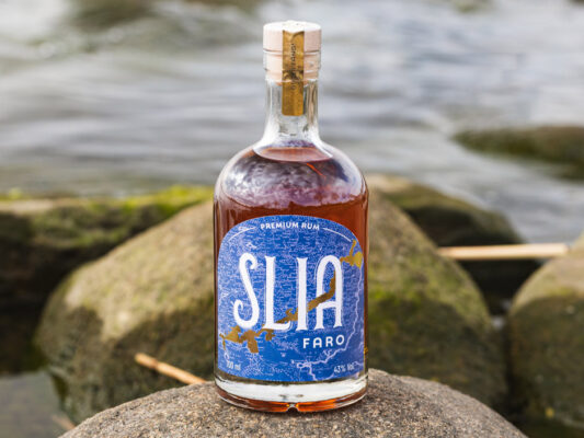 Slia Faro das Foto zeigt eine Flasche Slia Faro auf Felsen am Wasser