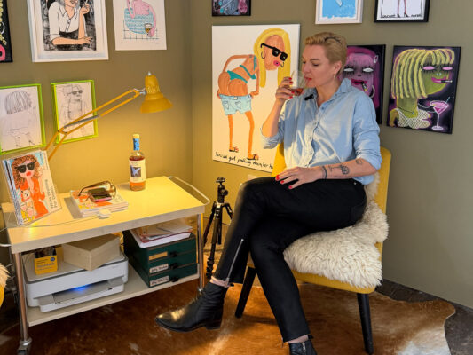 das Foto zeigt die Künstlerin Katharina Arndt in ihrem Atelier auf einem Stuhl beim Genuss eines Whiskeys