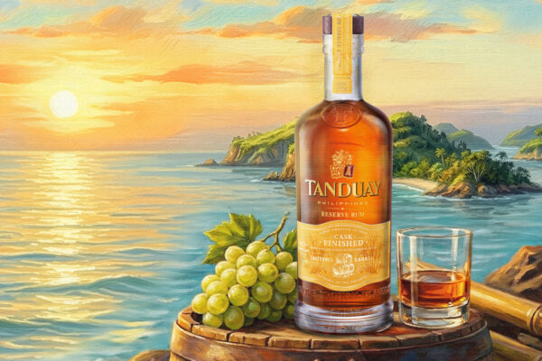 Tanduay Sauternes Cask Finish eine Flasche Tanduay Sauternes Cask Finish nebst Glas und Trauben auf einem Holzfass. Im Hintergrund Meer und eine INsel