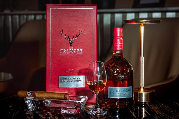 The Dalmore Cigar Malt Signature Reserve 18 Jahre eine Flasche The Dalmore Cigar Malt Signature Reserve 18 Jahre nebst Geschenkhülle, Glas und Zigarre auf einem Tisch vor einem Sessel